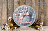a decorative round sign with a floral design, surrounded by flowers and placed on a wooden surface.