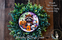 A Halloween-themed wreath featuring a raccoon wearing a costume, surrounded by pumpkins, skulls, and other spooky elements.