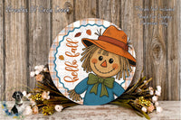 a round, decorative sign with a scarecrow illustration, surrounded by a floral arrangement and placed on a wooden surface.