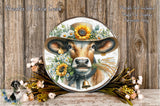 A decorative plate featuring a cow wearing a sunflower hat, surrounded by flowers and a bell, placed on a wooden surface.