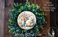 a wreath with a white rabbit and Easter eggs, surrounded by a lush green wreath. The wreath is displayed on a wooden surface, and there is a small dog in the bottom right corner of the image.