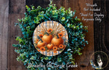 a wreath made of various autumn-themed elements, including pumpkins, flowers, and greenery, set against a wooden background.