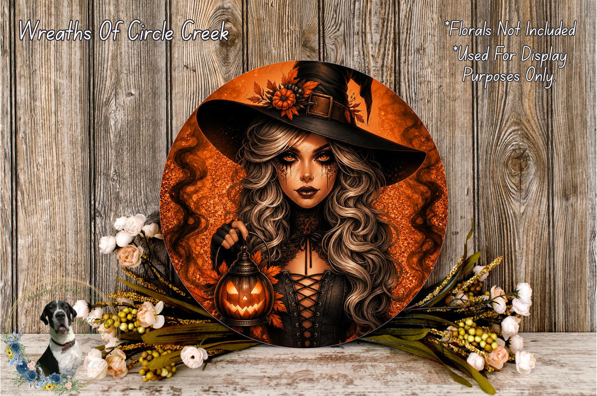 a woman with long, wavy hair wearing a witch's hat and holding a carved pumpkin, surrounded by a floral arrangement and a wooden background.