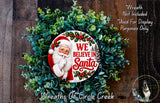 A wreath made of green foliage and featuring a Santa Claus image, with the text "We Believe in Santa" displayed on it.