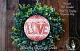A wreath made of green leaves and a red and white circular sign with the word "LOVE" written on it.