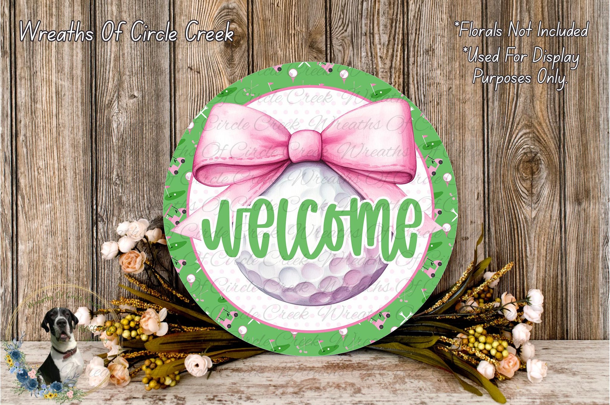 a round sign with a pink bow, surrounded by a floral arrangement and a wooden background.