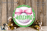 a round sign with a pink bow, surrounded by a floral arrangement and a wooden background.