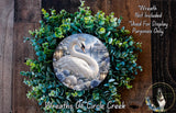A wreath made of green leaves and a white swan, with a circular image of a snowy landscape in the center.