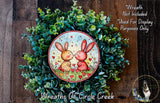 A wreath made of green plants and featuring two rabbits with hearts around them.