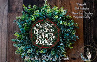 A Christmas wreath made of green leaves and a red and white circular sign that says "May Your Christmas Be Furry & Bright".
