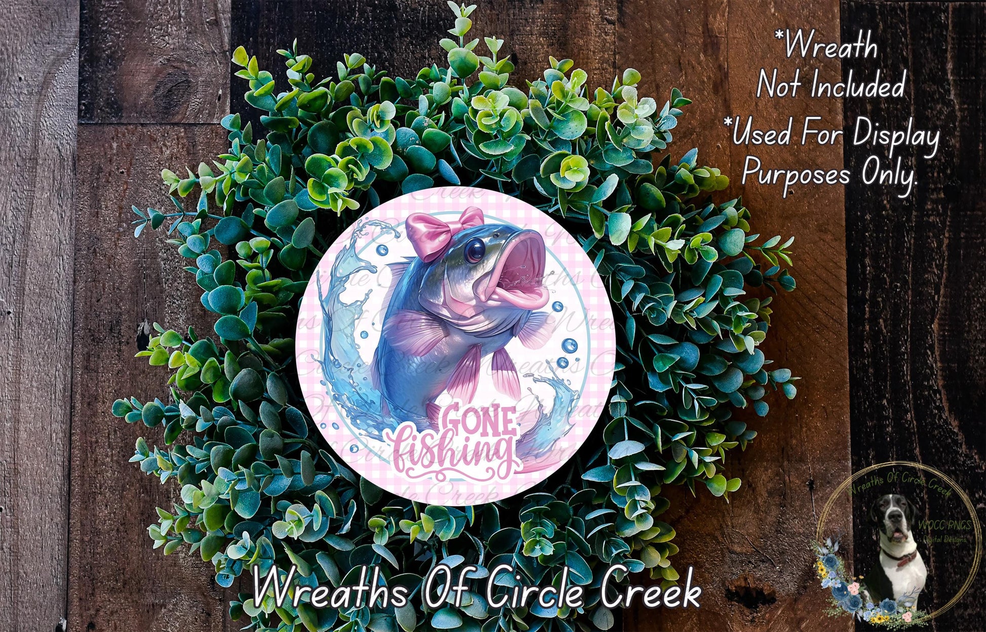 a wreath made of green foliage and a circular design with a fish and the text "Gone Fishing" on it. The wreath is displayed on a wooden surface, and there is a small dog visible in the bottom right corner of the image.