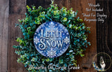 A wreath made of green leaves and branches, with a blue circular sign that says "Let it snow" in the center.