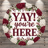 A circular sign with the text "YAY! you're here" surrounded by a floral border of red and white flowers.