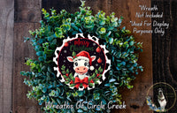 a Christmas wreath with a cow wearing a Santa hat, surrounded by greenery. The wreath is displayed on a wooden background, and there is a text overlay that reads "Merry Christmas" and "Not included for display purposes only".