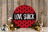 a red circular sign with the word "LOVE SHACK" written on it, surrounded by a floral arrangement and a wooden background.