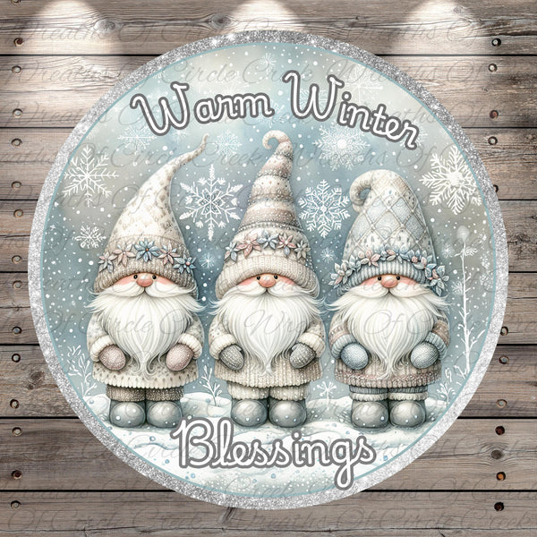 A circular design featuring three gnomes wearing winter clothing and hats, with snowflakes and the text "Warm Winter Blessings" written above them.