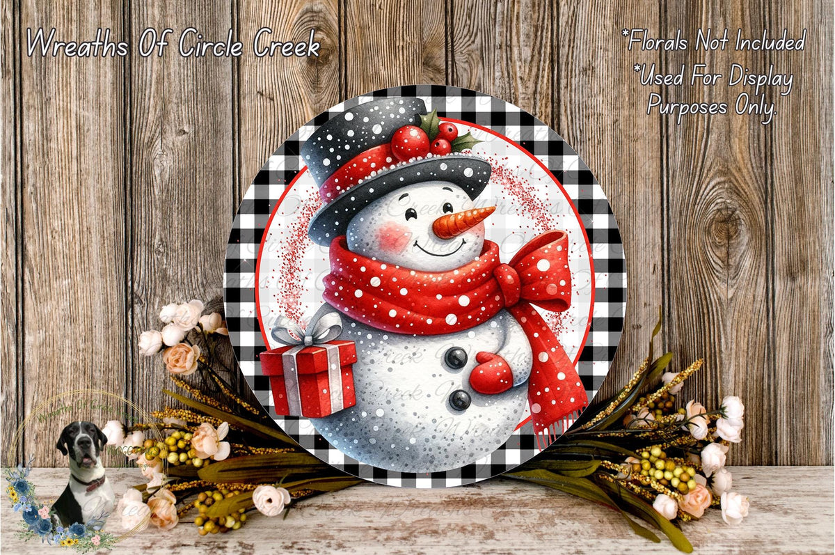 A snowman wearing a red scarf and hat, holding a red gift box, is surrounded by a wreath of flowers and a wooden background.