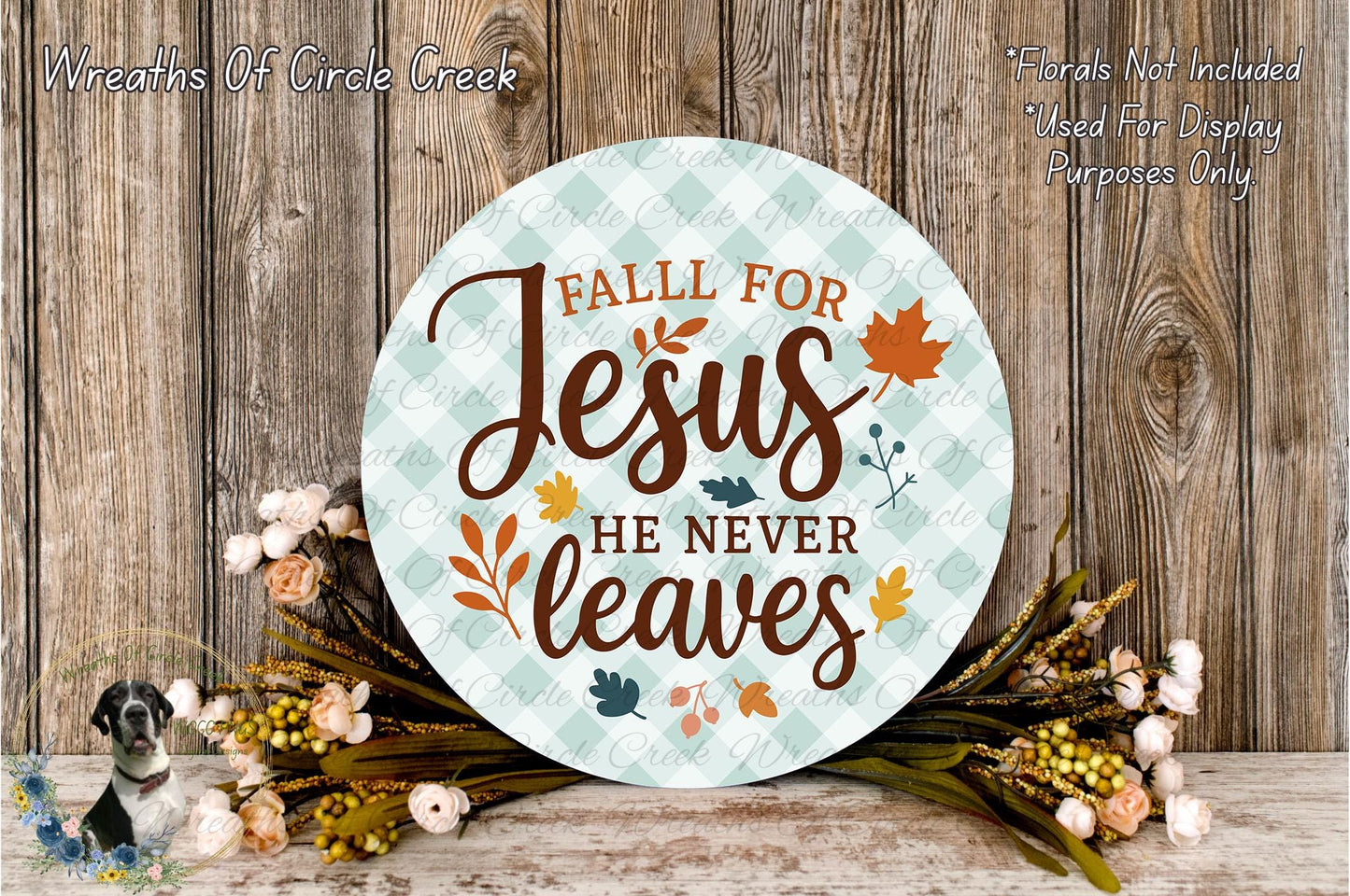 a round sign with the text "Fall for Jesus he never leaves" surrounded by autumn leaves and flowers, placed on a wooden surface.