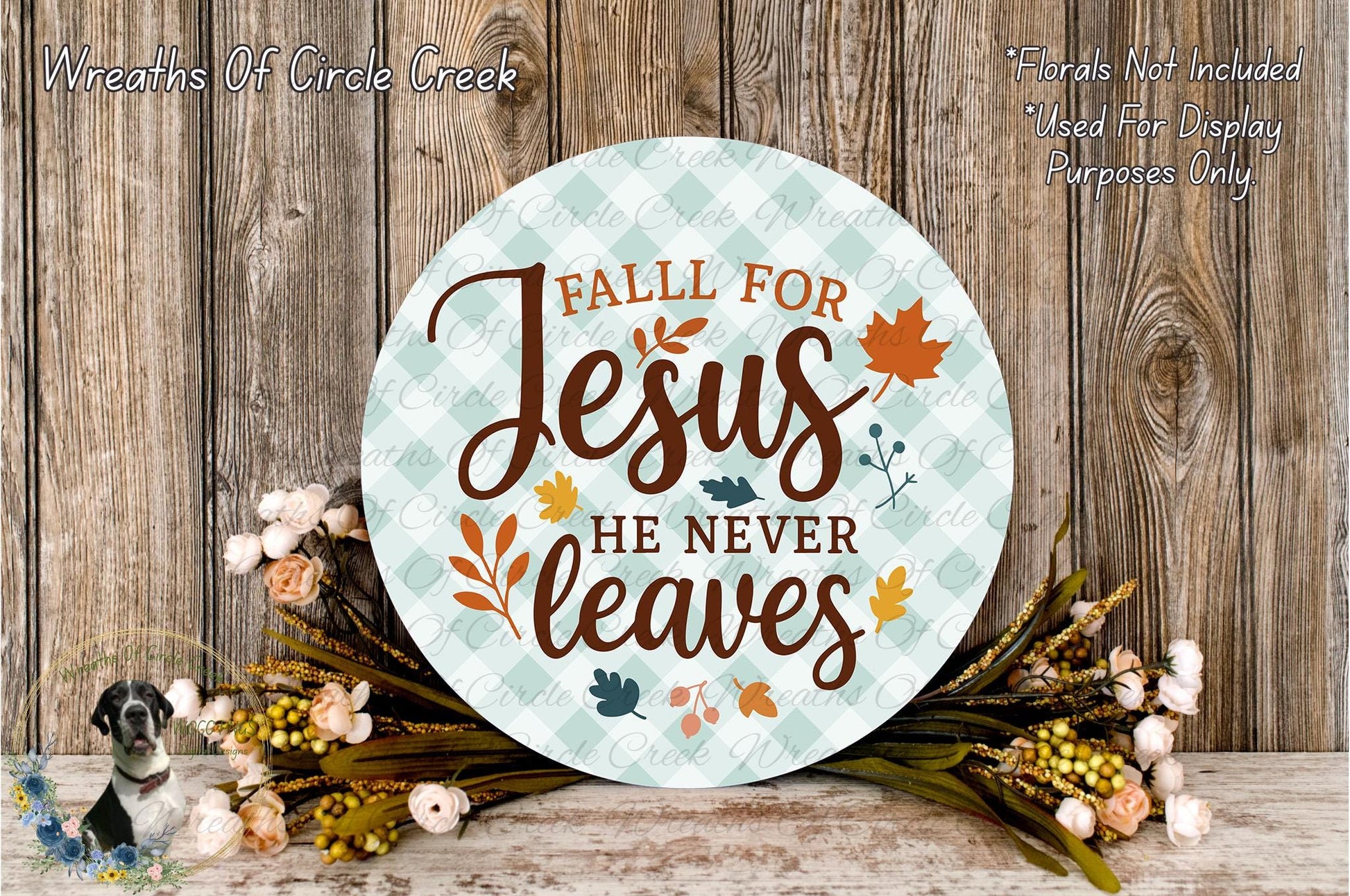a round sign with the text "Fall for Jesus he never leaves" surrounded by autumn leaves and flowers, placed on a wooden surface.