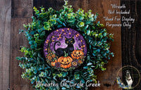 A Halloween-themed wreath made of green foliage and featuring a black cat, pumpkins, and a purple background.