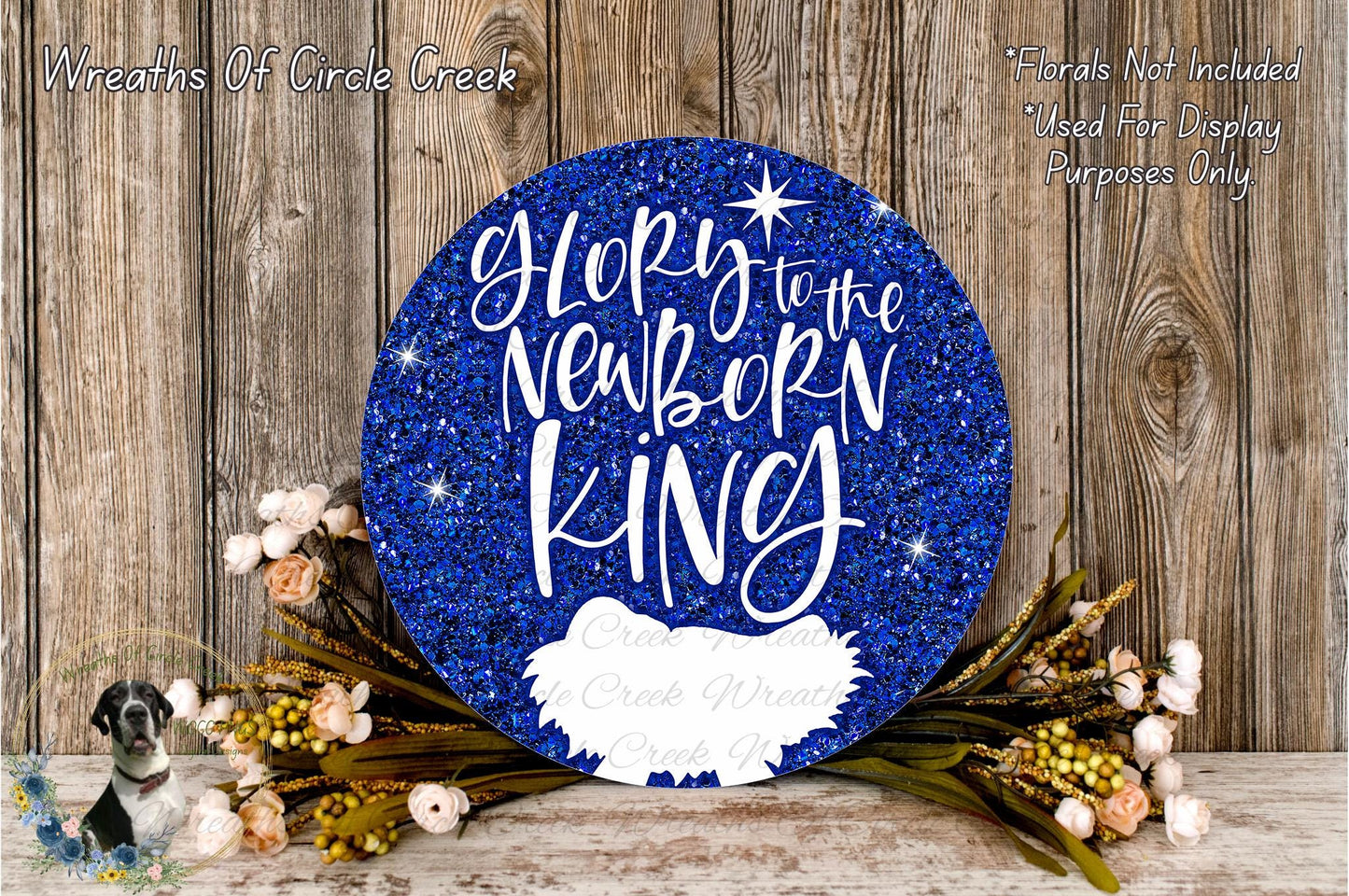 a blue glitter sign with the text "Glory to the Newborn King" and a small white bird image. The sign is surrounded by a wreath of flowers and placed on a wooden surface.