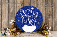 a blue glitter sign with the text "Glory to the Newborn King" and a small white bird image. The sign is surrounded by a wreath of flowers and placed on a wooden surface.