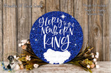 a blue glitter sign with the text "Glory to the Newborn King" and a small white bird image. The sign is surrounded by a wreath of flowers and placed on a wooden surface.