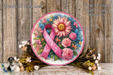 A decorative wreath with a pink ribbon, surrounded by various flowers and foliage, placed on a wooden surface.