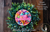 a colorful wreath made of green foliage and decorated with various sweets, including a large pink and purple sign that says "SWEET SUMMERTIME".