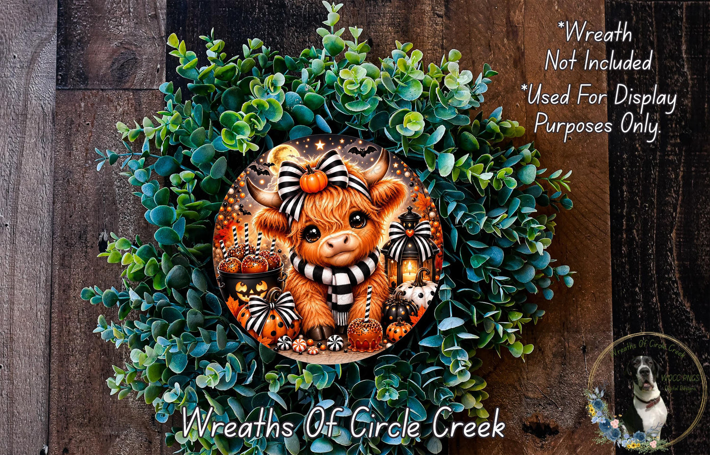a wreath with a cow wearing a black and white scarf, surrounded by green foliage and various decorative elements such as pumpkins and lanterns.