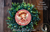 A wreath made of green leaves and flowers, with a red and white checkered border and a cherub figure in the center. The cherub is smiling and holding a heart.