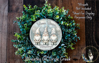 A wreath made of green leaves and topped with three gnome figurines, with a silver plaque in the center that reads "Wreath Not Included * Used For Display Purposes Only. * Wreaths of Circle Creek".