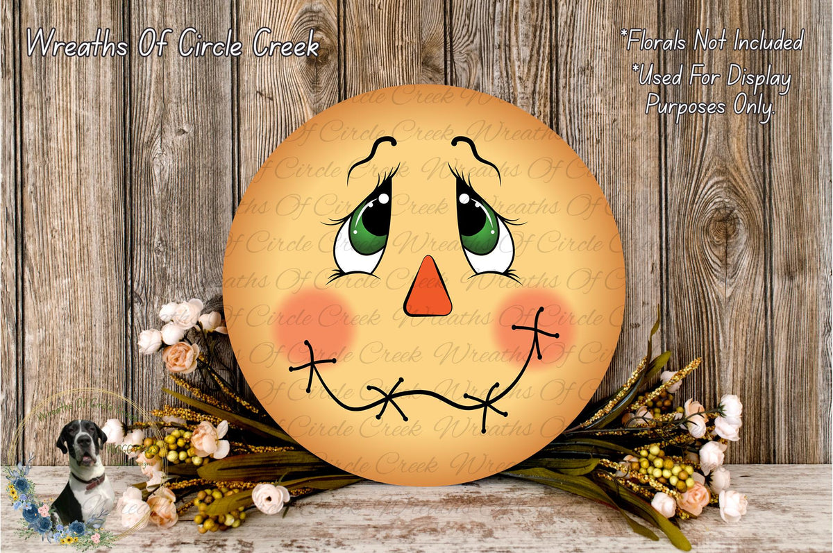 a round wooden sign with a face painted on it, surrounded by flowers and placed on a wooden surface.