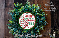 a Christmas wreath made of green and white leaves, with a red and white circular sign that reads "Rockin' Around the Christmas Tree".
