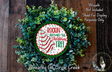 a Christmas wreath made of green and white leaves, with a red and white circular sign that reads "Rockin' Around the Christmas Tree".