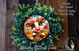 a wreath with a cow and fall-themed decorations, including pumpkins and sunflowers, set against a wooden background.