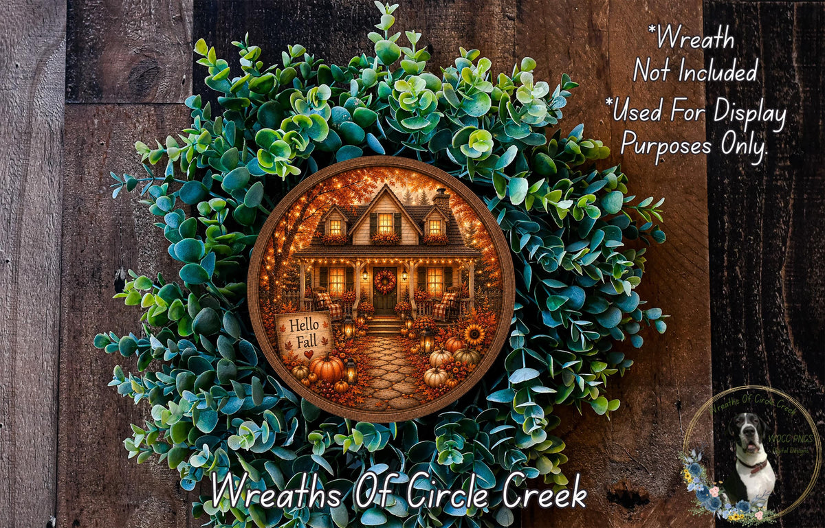 A wreath with a house and autumn decorations, including pumpkins and sunflowers, is displayed on a wooden surface.