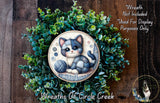 A wreath made of green leaves and a cat illustration, with the word "Hello" written below the cat.