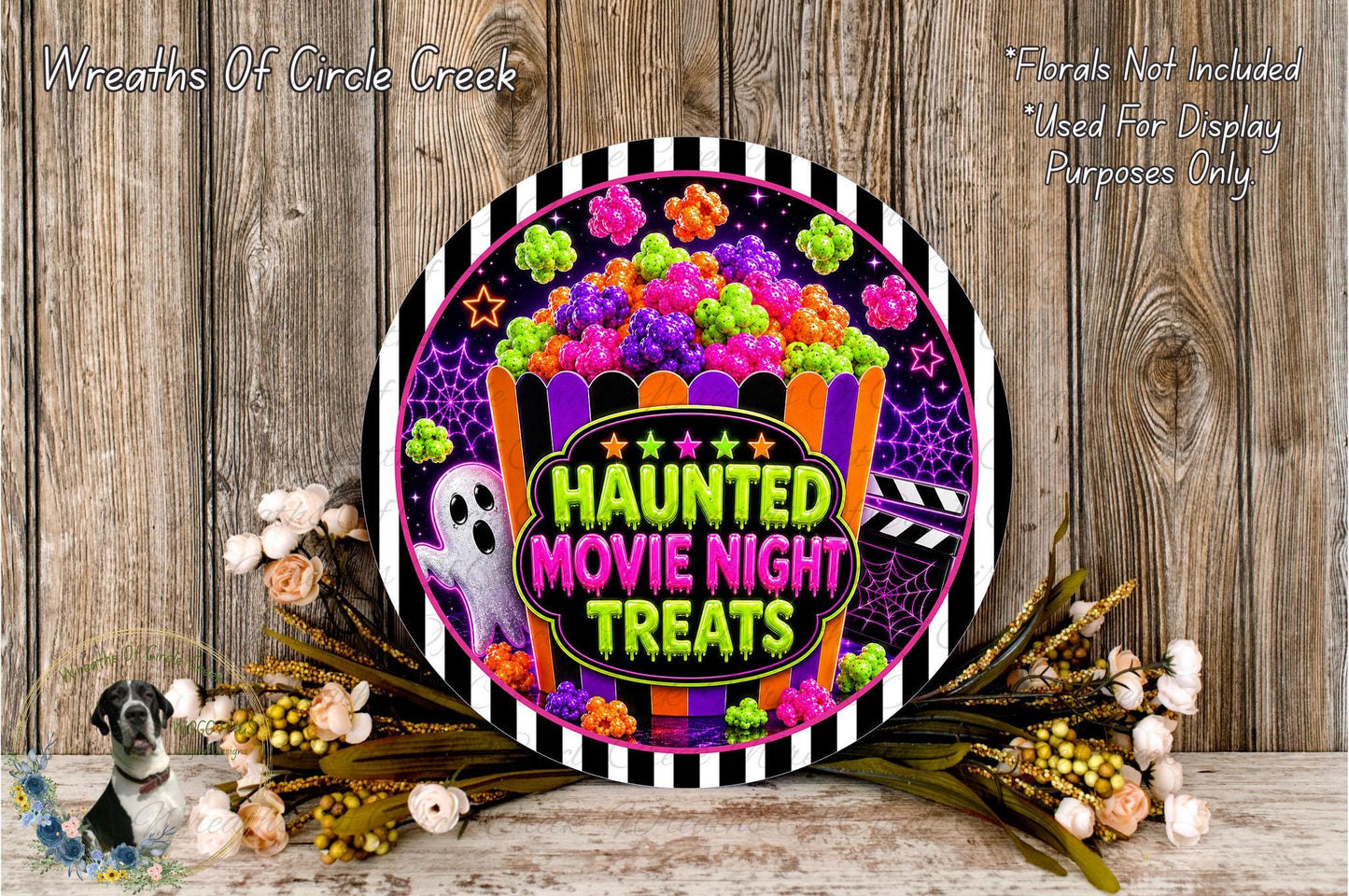 a Halloween-themed decoration with a ghost, a bucket of candy, and a sign that says "Haunt Movie Night Treats". The decoration is set against a wooden background, and there are some flowers and greenery surrounding it.
