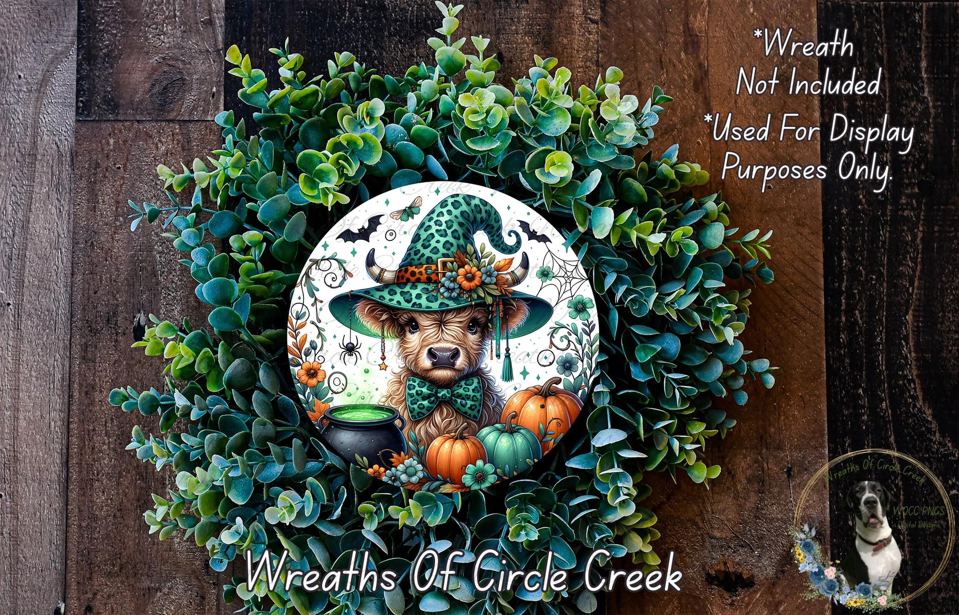 a wreath with a cow wearing a witch's hat, surrounded by various autumn-themed elements such as pumpkins, gourds, and a cauldron. The wreath is displayed on a wooden surface, and there is a small dog in the bottom right corner of the image.