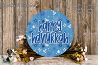 A circular sign with the text "happy Hanukkah" in blue and white, surrounded by a floral arrangement and a wooden background.