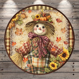 A decorative round frame with a scarecrow figure wearing a plaid shirt, hat, and bow, surrounded by autumn leaves, sunflowers, and a pumpkin.