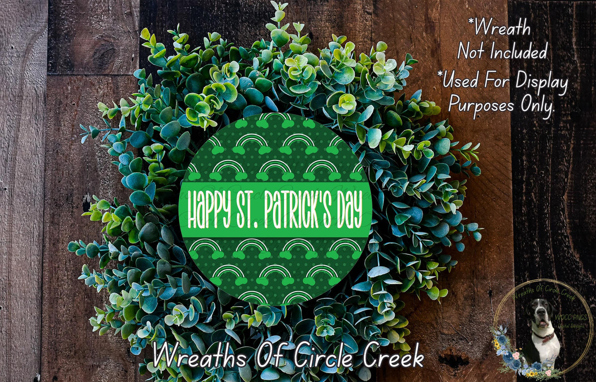 a wreath made of green leaves and flowers, with a circular design in the center that says "Happy St. Patrick's Day". The wreath is displayed on a wooden surface, and there is a small dog in the bottom right corner.