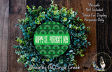 a wreath made of green leaves and flowers, with a circular design in the center that says "Happy St. Patrick's Day". The wreath is displayed on a wooden surface, and there is a small dog in the bottom right corner.