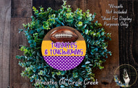 a wreath made of green foliage and a football, with the text "Tailgates & Touchdowns" written on it. The wreath is displayed on a wooden surface, and there is a small dog in the bottom right corner of the image.