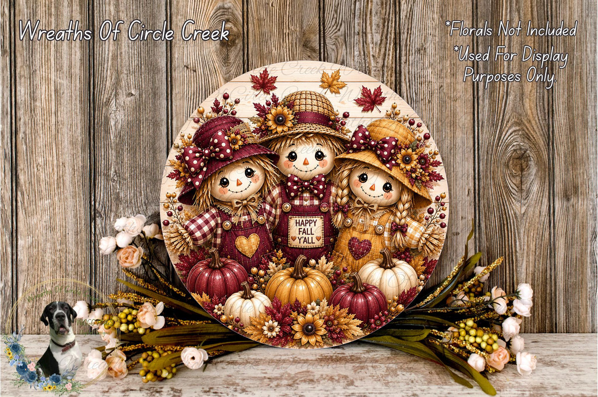 A decorative wreath featuring three scarecrow-like figures, each holding a pumpkin, surrounded by autumn foliage and flowers. The wreath is displayed on a wooden surface, with a text overlay providing information about the wreath's purpose.