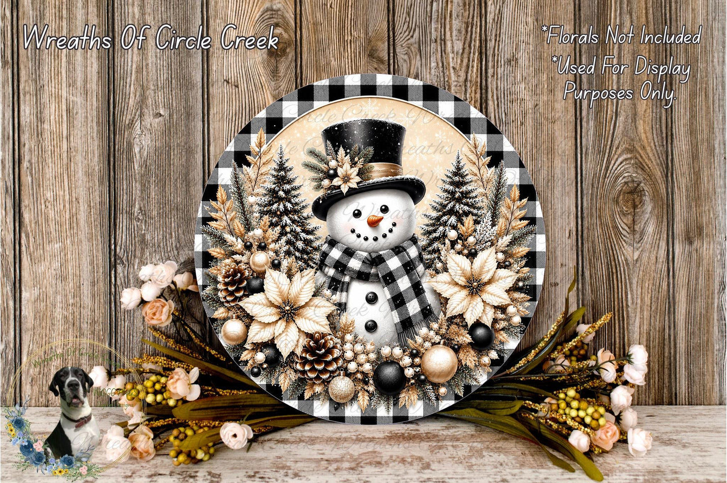 A snowman decoration with a black top hat, surrounded by a wreath of pine trees, flowers, and ornaments, placed on a wooden surface.