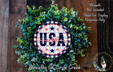 a wreath made of green leaves and a circular sign with the text "USA" on it, placed on a wooden surface.