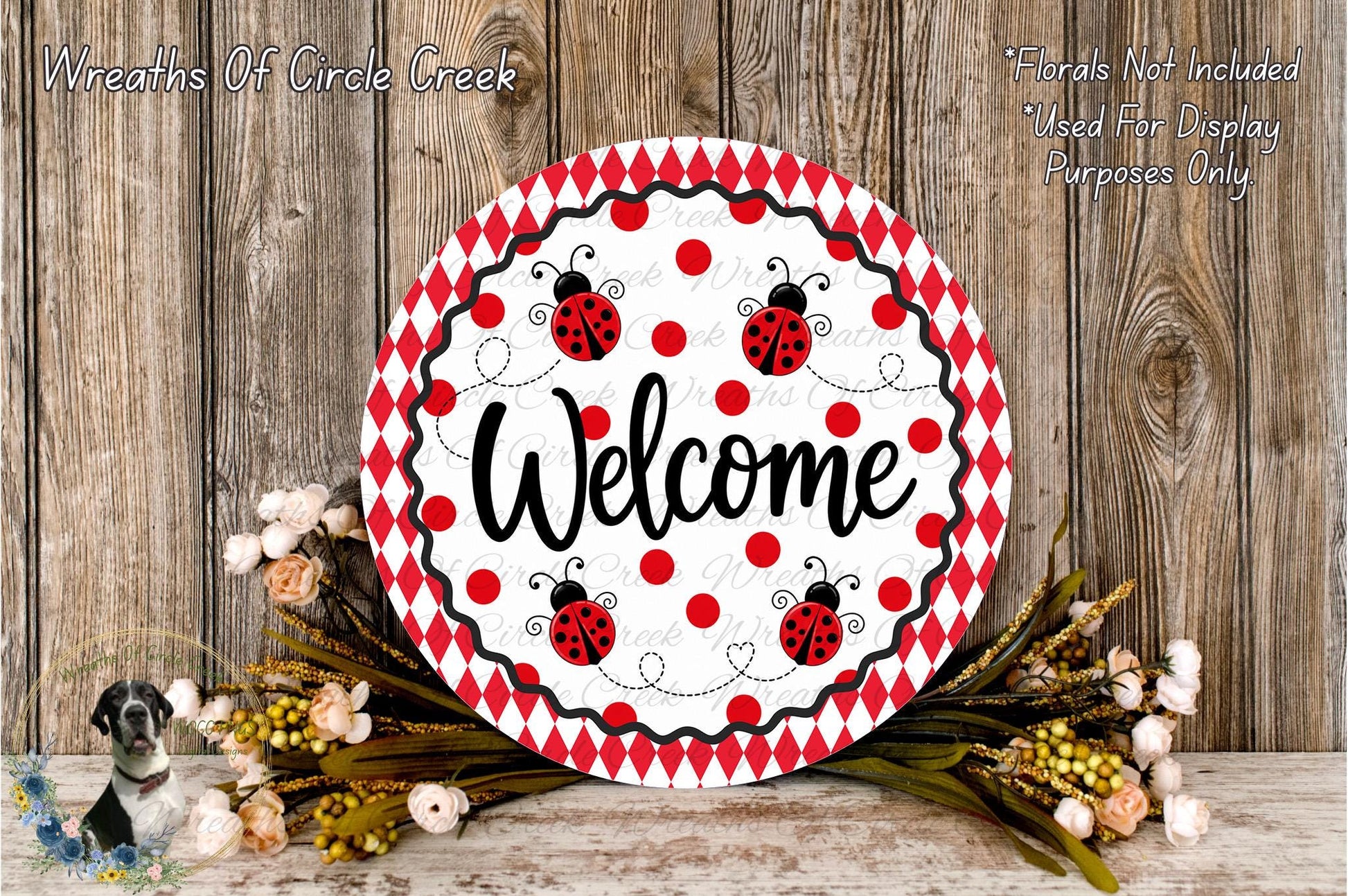 a decorative welcome sign with a red and white polka dot pattern, surrounded by a floral arrangement and a wooden background.