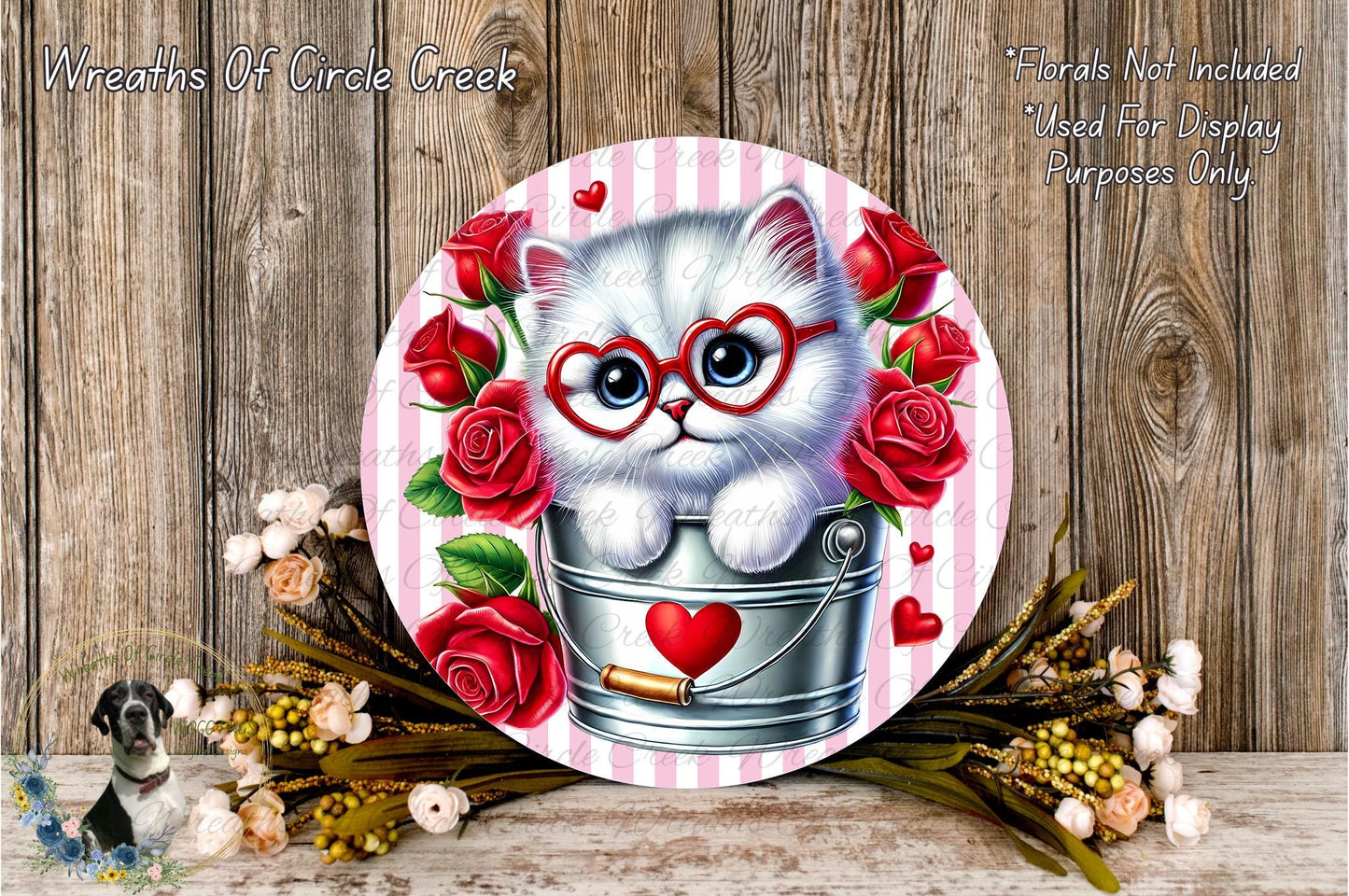 A white cat wearing red glasses is sitting in a metal bucket, surrounded by red roses and a heart-shaped decoration.